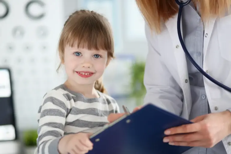 Young girl smiling next to a clinician holding a clipboard