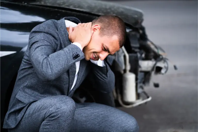 Man crouched beside a damaged car holding the back of his neck