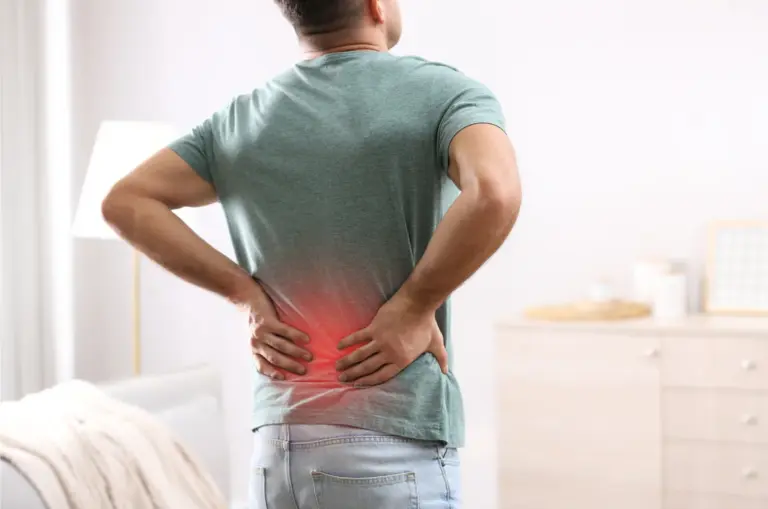 Man standing at home with both hands on a painful lower back
