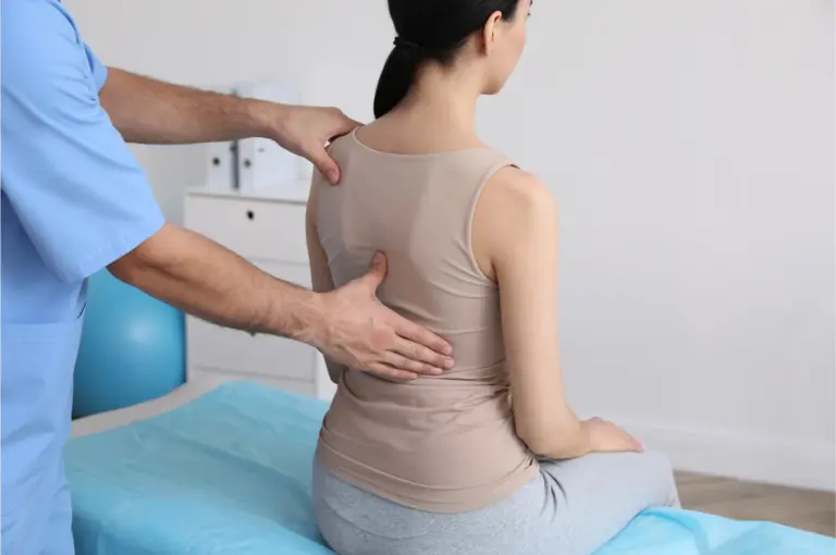 Clinician assessing the mid back of a seated patient in a treatment room